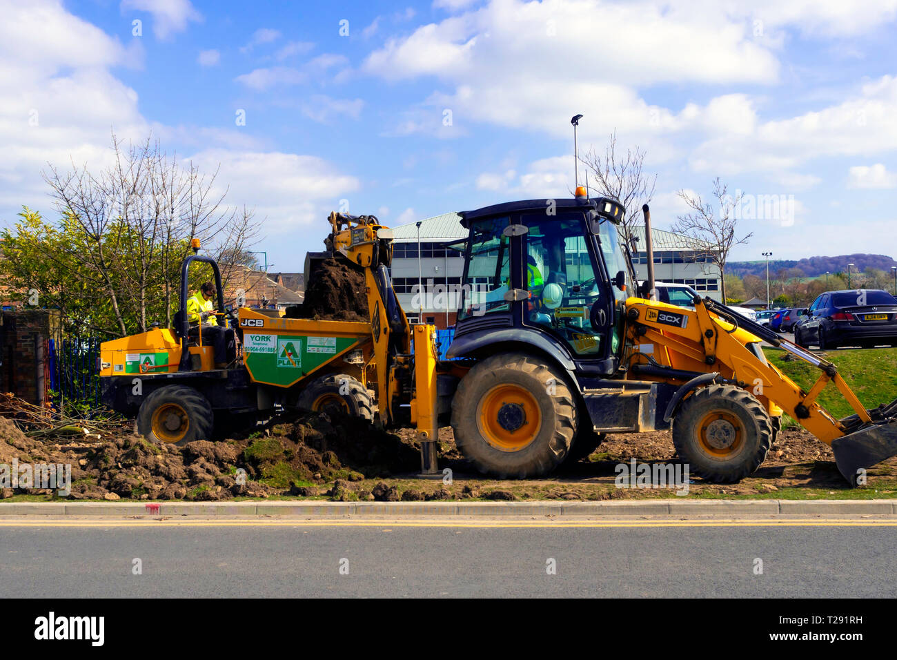 Workmen using a JCB 3CX excavator loading excavated topsoil into a dumper truck for removal Stock Photo