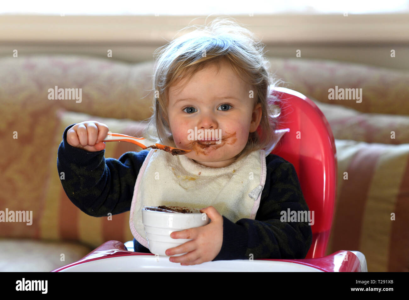 Baby girl feeding herself with chocolate on her face Stock Photo