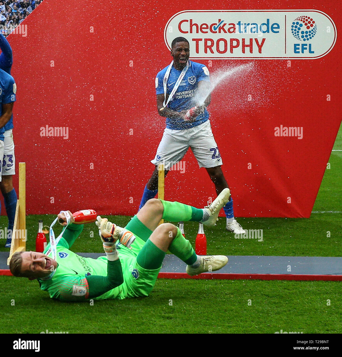London, UK. 31st Mar, 2019. Checkatrade Trophy Final, Portsmouth versus Sunderland; Craig MacGillivray of Portsmouth takes a tumble after knocking the hoarding down with Omar Bogle of Portsmouth spraying champagne in celebration Credit: Action Plus Sports/Alamy Live News Stock Photo