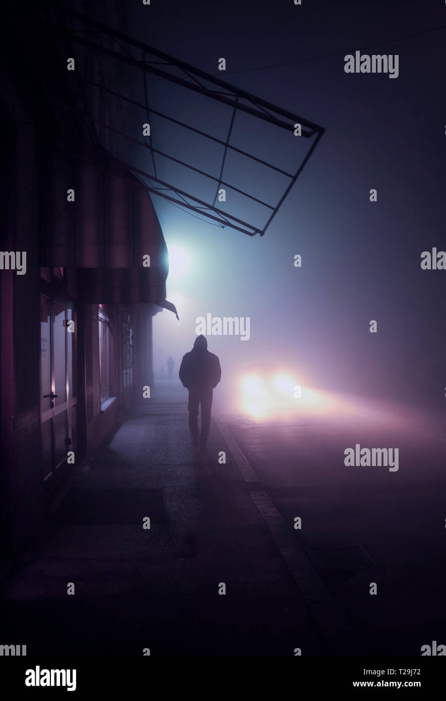 Silhouette of a young man walking on sidewalk in a city on a foggy ...