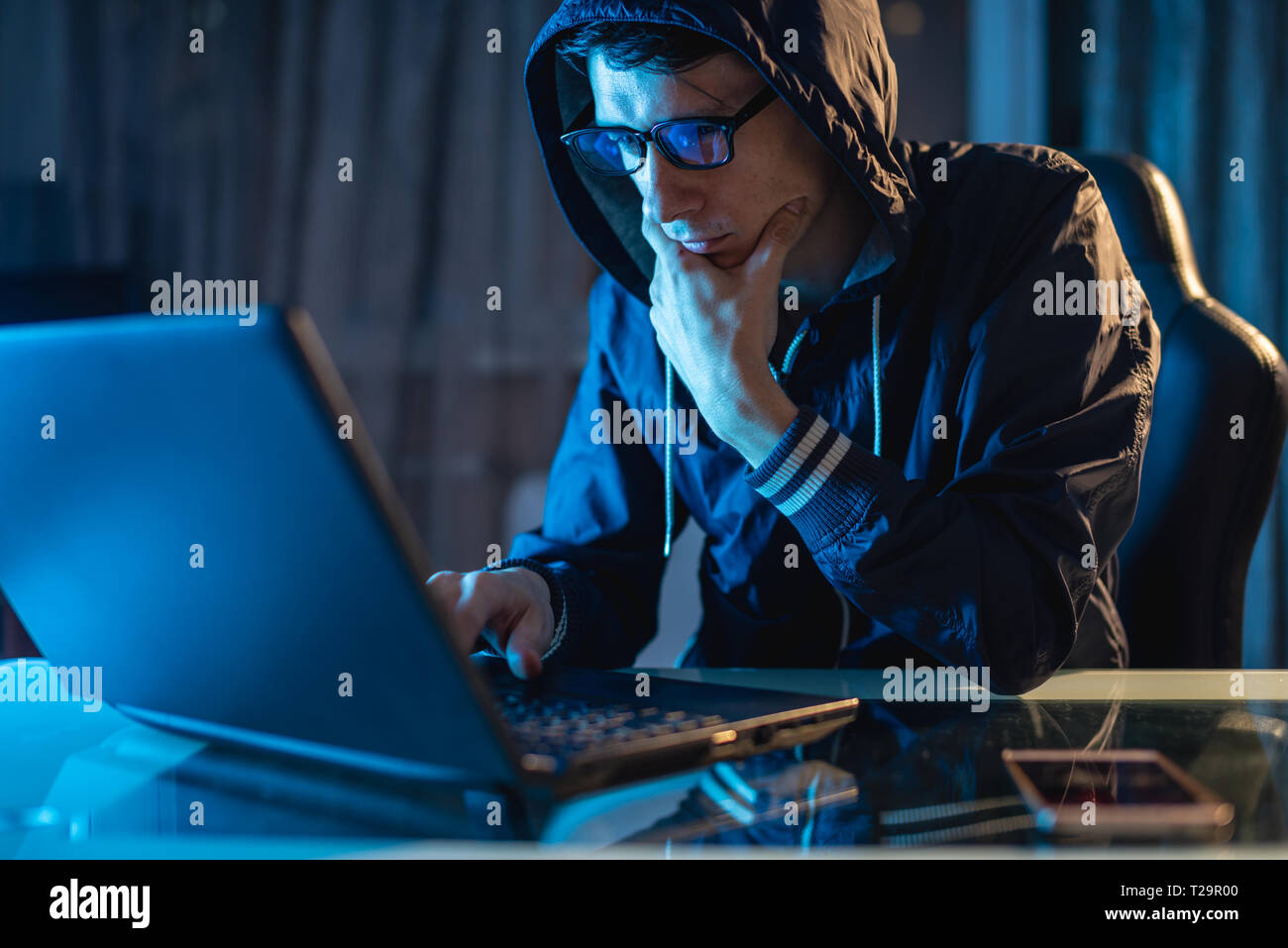 Cybercriminal hacker in the hood typing program code while stealing access databases with passwords. The concept of cyber security Stock Photo
