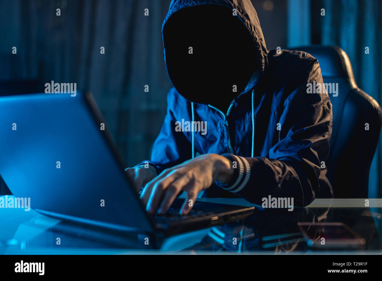 Anonymous hacker programmer uses a laptop to hack the system in the dark. Creation and infection of malicious virus. The concept of cybercrime and hac Stock Photo