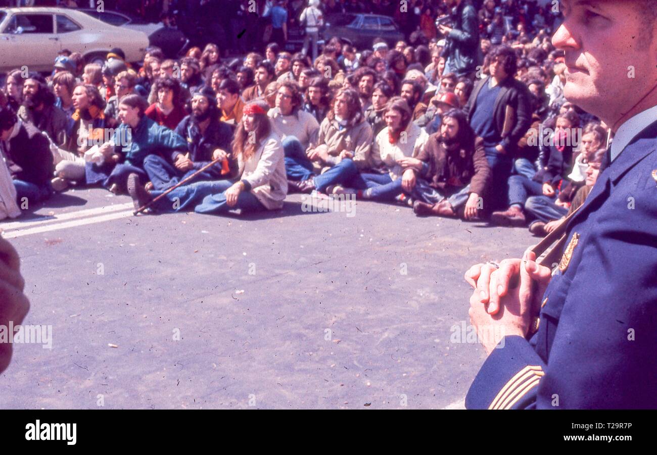 During the 1971 May Day Protests against the Vietnam War, a large number of protesters in hippie attire engage in a sit in as a police officer stands in the foreground, in Washington, DC, May 1971. () Stock Photo