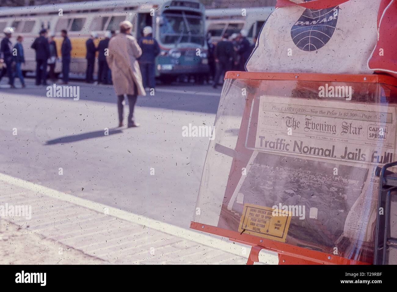 During the May Day protests against the Vietnam War in Washington, DC, a newspaper kiosk for the Evening Star is visible with headline reading Traffic Normal, Jails Full, while police officers load protesters into buses in the background, 1971. () Stock Photo