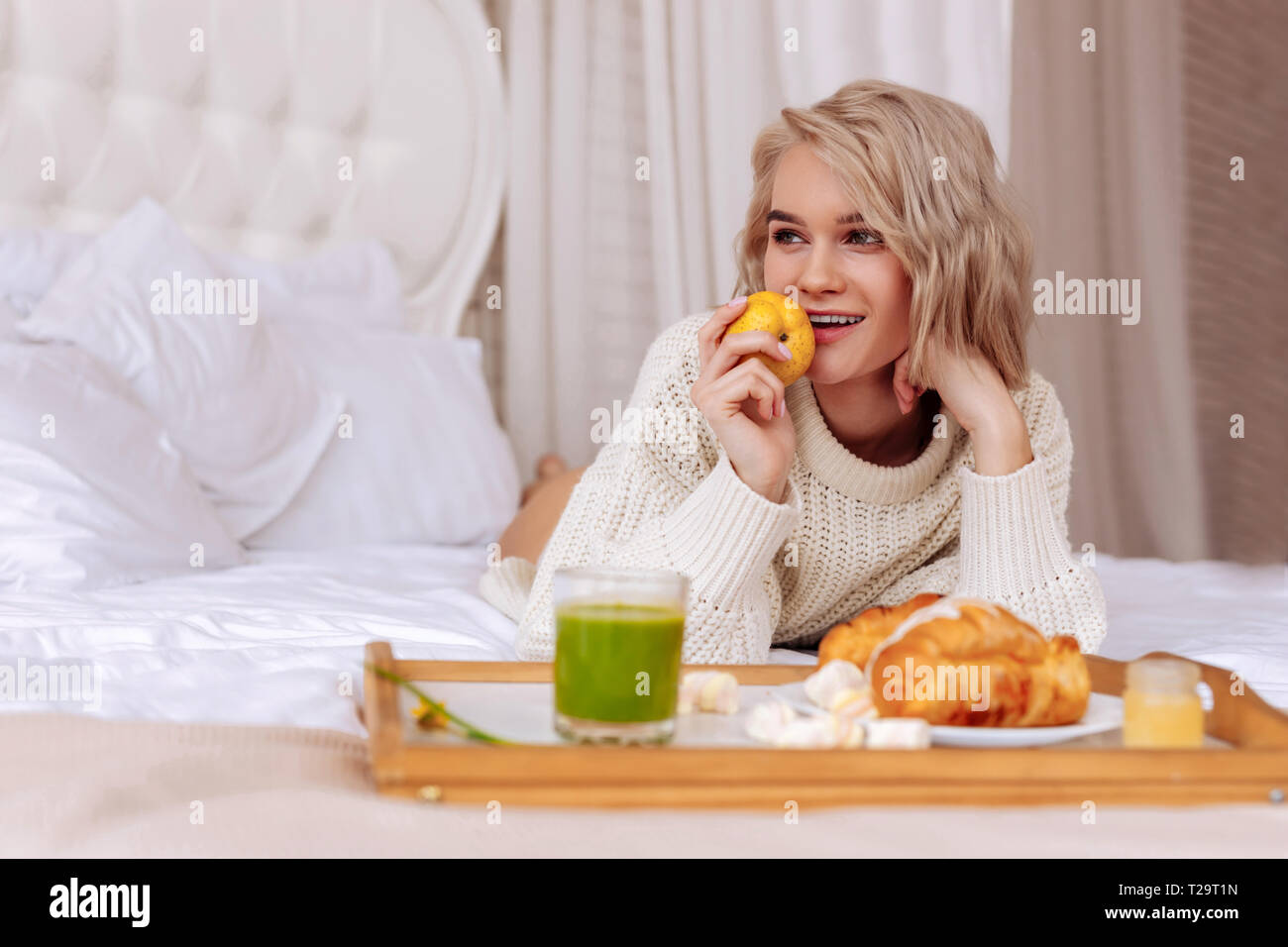 Dark-eyed woman chilling on bed and holding little apple Stock Photo