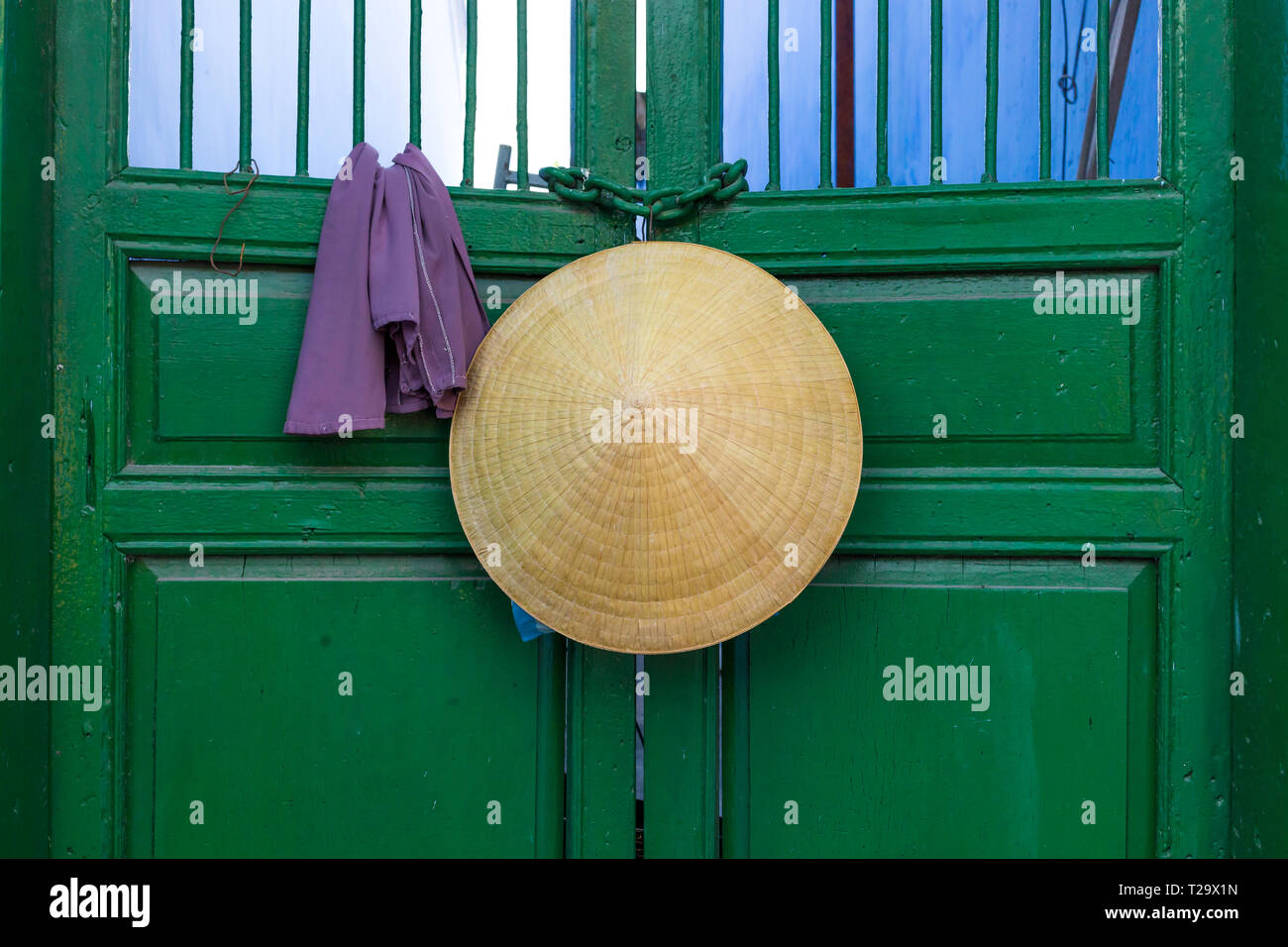 Asian style conical hat hanging on a green door in Vietnam . Stock Photo