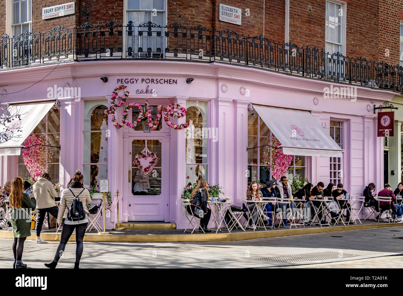 People sitting outside Peggy Porschen Cakes, in Belgravia , a cake shop known for its striking pastel pink exterior, London, UK Stock Photo
