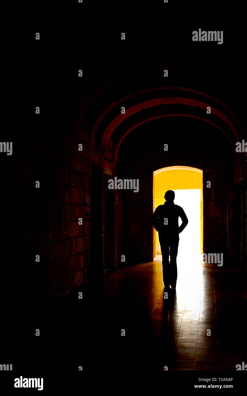 Lone figure, silhouetted, walking through a dark corridor. Stock Photo