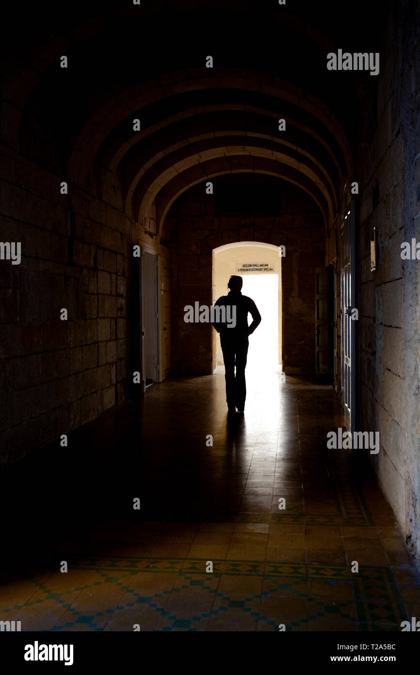 Lone figure, silhouetted, walking through a dark corridor. Stock Photo