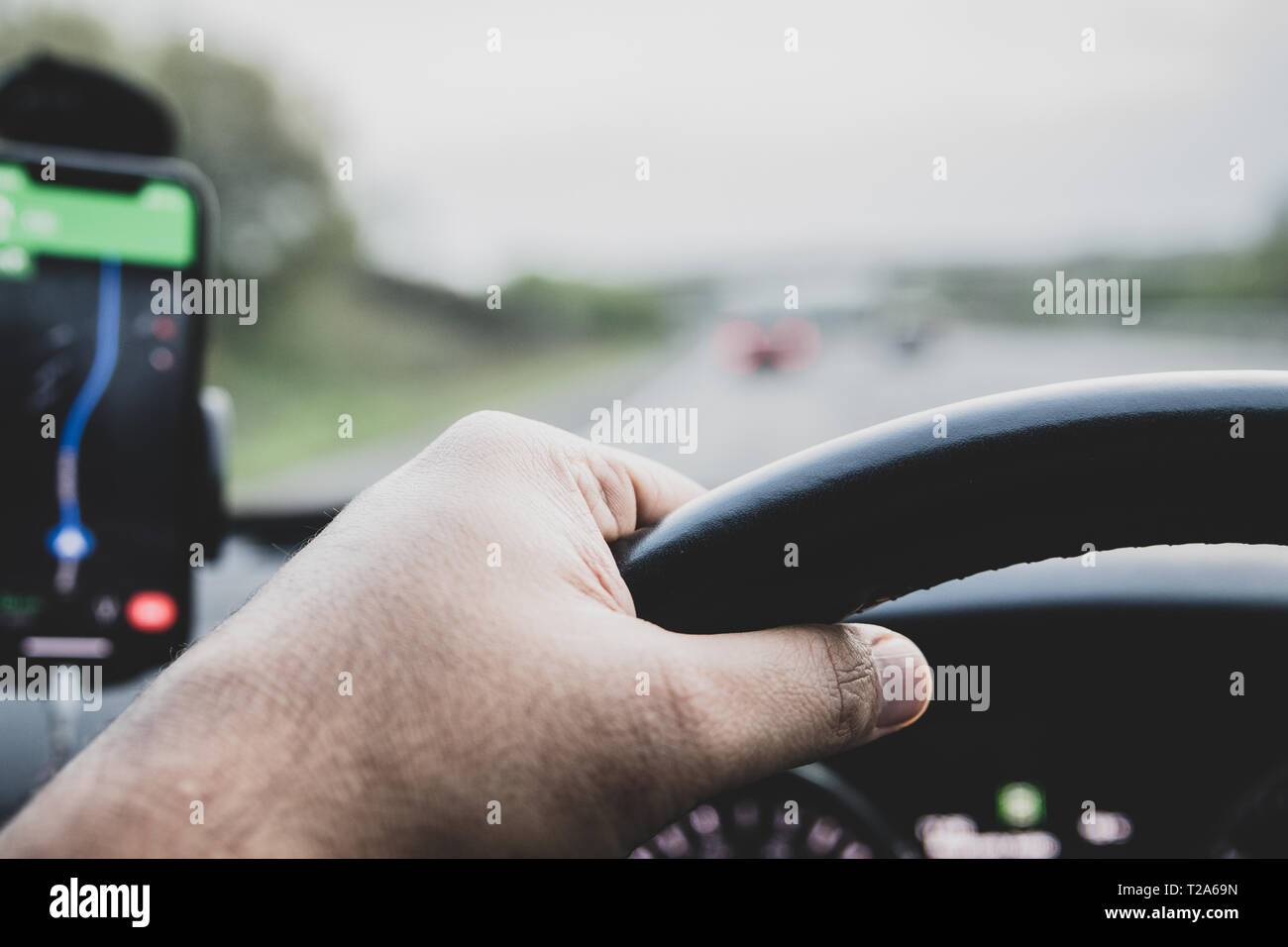 Google maps on a smart phone attached to holder on the windsceen of a car - seen by the driver - with a view of hands on steering wheel. Stock Photo