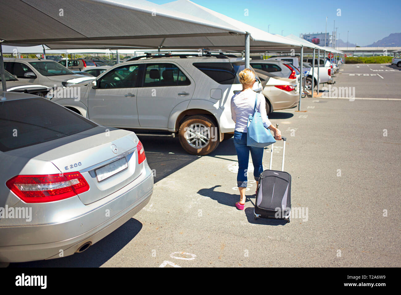 Woman walking with suitcase to car, Cape Town International Airport Stock Photo