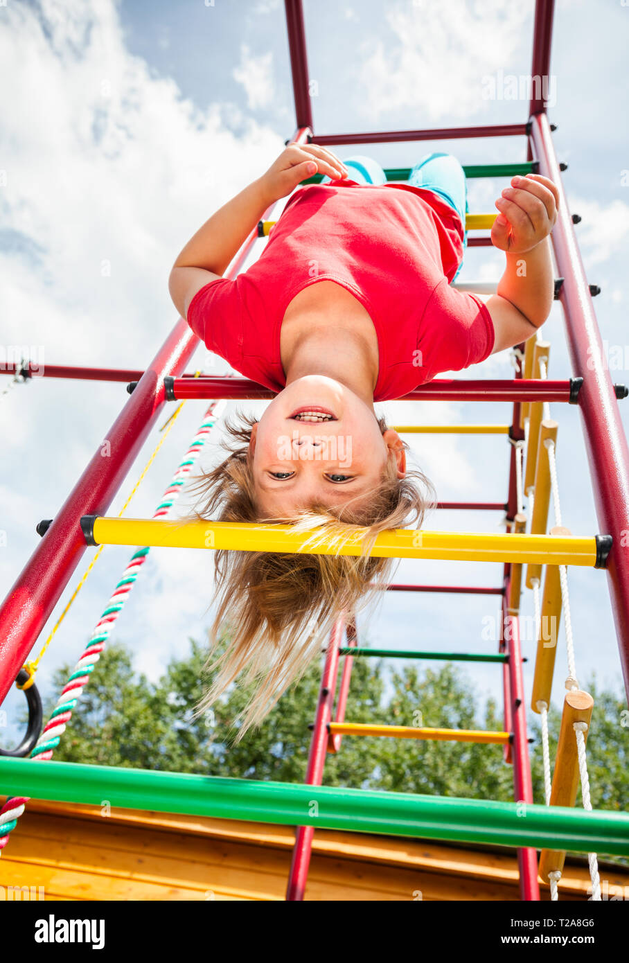 Elementary age girl hanging from a jungle gym (monkey bars or climbing frame) while playing in a playground - child safety or risky play concept Stock Photo