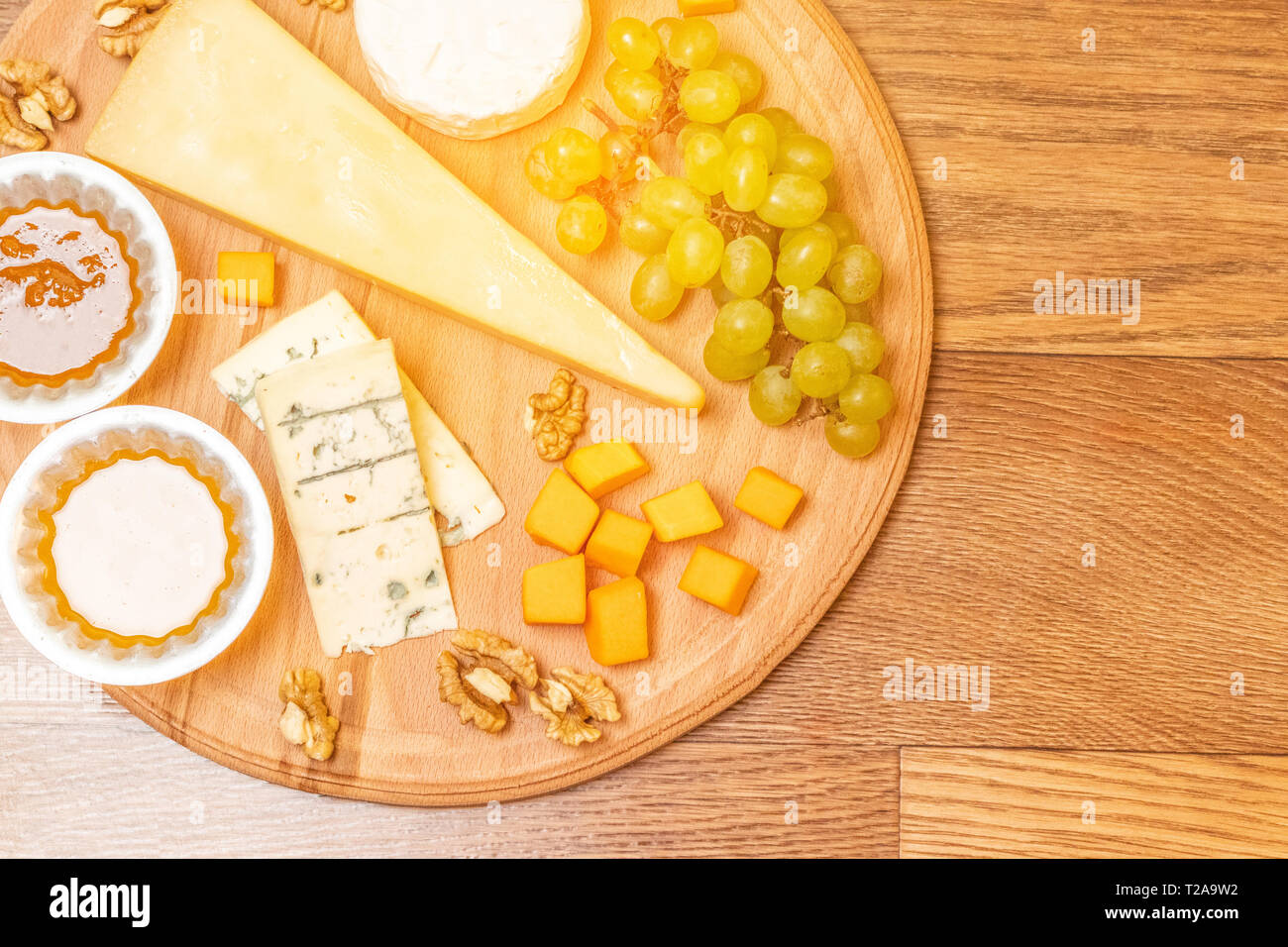 Assorted cheese on a round wooden plate Camembert cheese, slices of hard cheese, walnuts, grapes