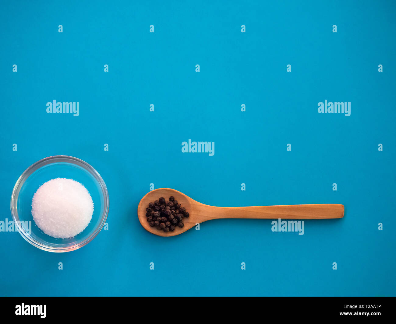 Crystal bowl with common marine salt and a wooden spoon with black peppercorns on a blue background Stock Photo