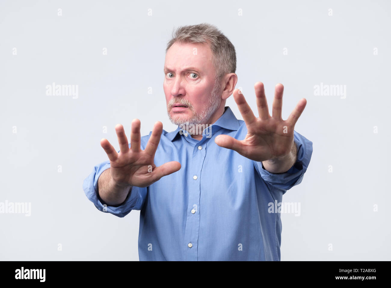 Mature european man in blue shirt and glasses showing refusal gesture. It is not for me, leave me in piece, has angry expression. Studio shoot Stock Photo