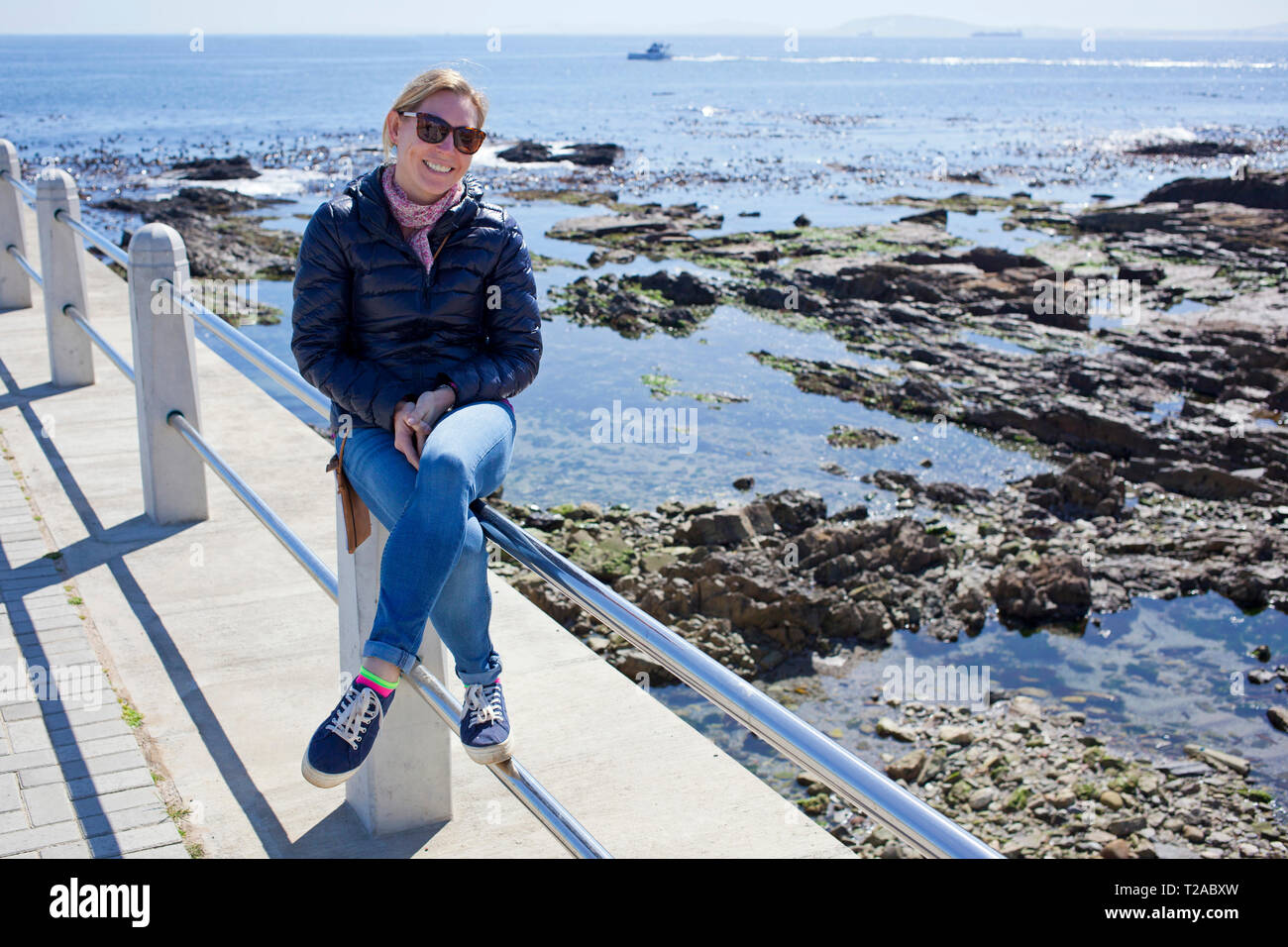 Woman sitting on railing along Sea Point Promenade, Cape Town Stock Photo