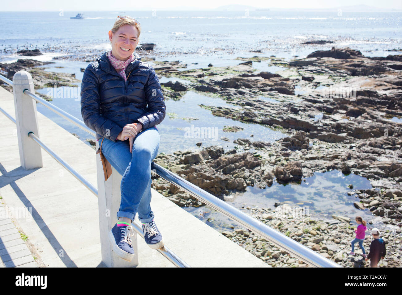 Woman sitting on railing along Sea Point Promenade, Cape Town Stock Photo