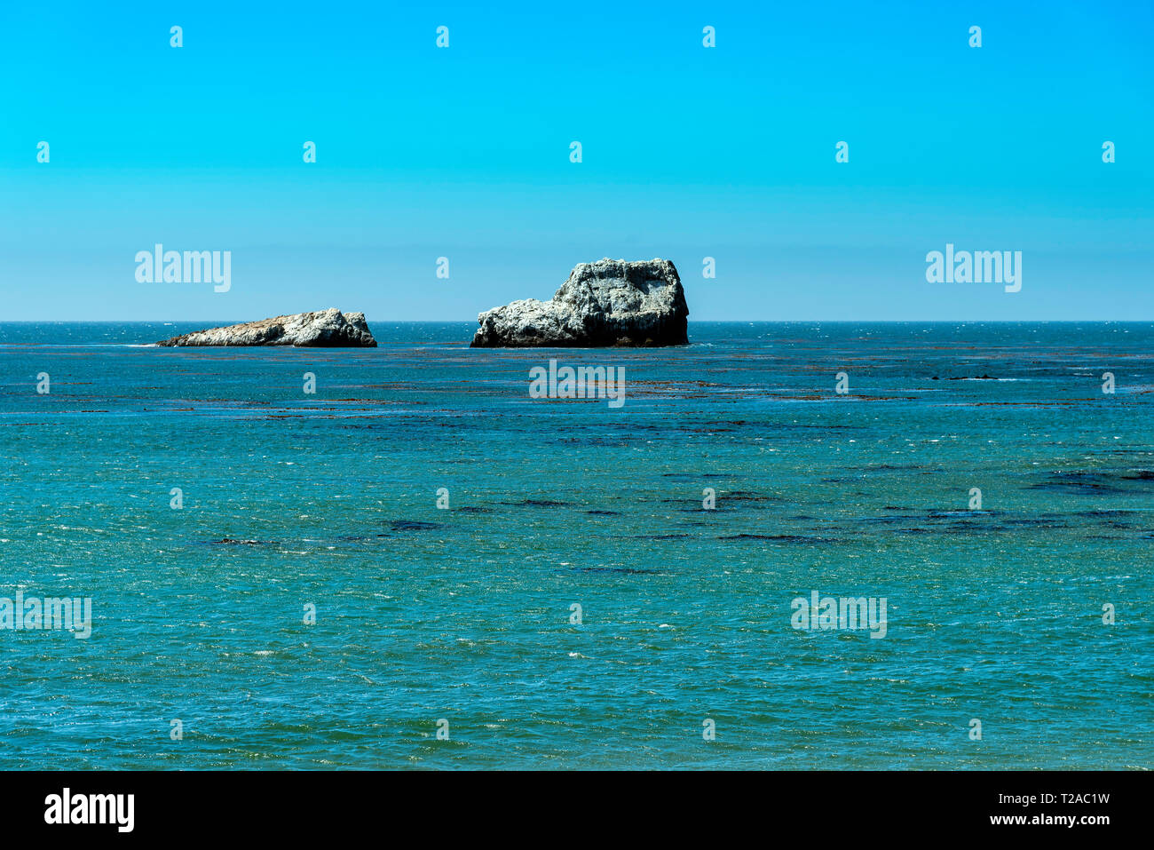 Overlooking ocean with rocky formations in sea under bright blue sky. Stock Photo