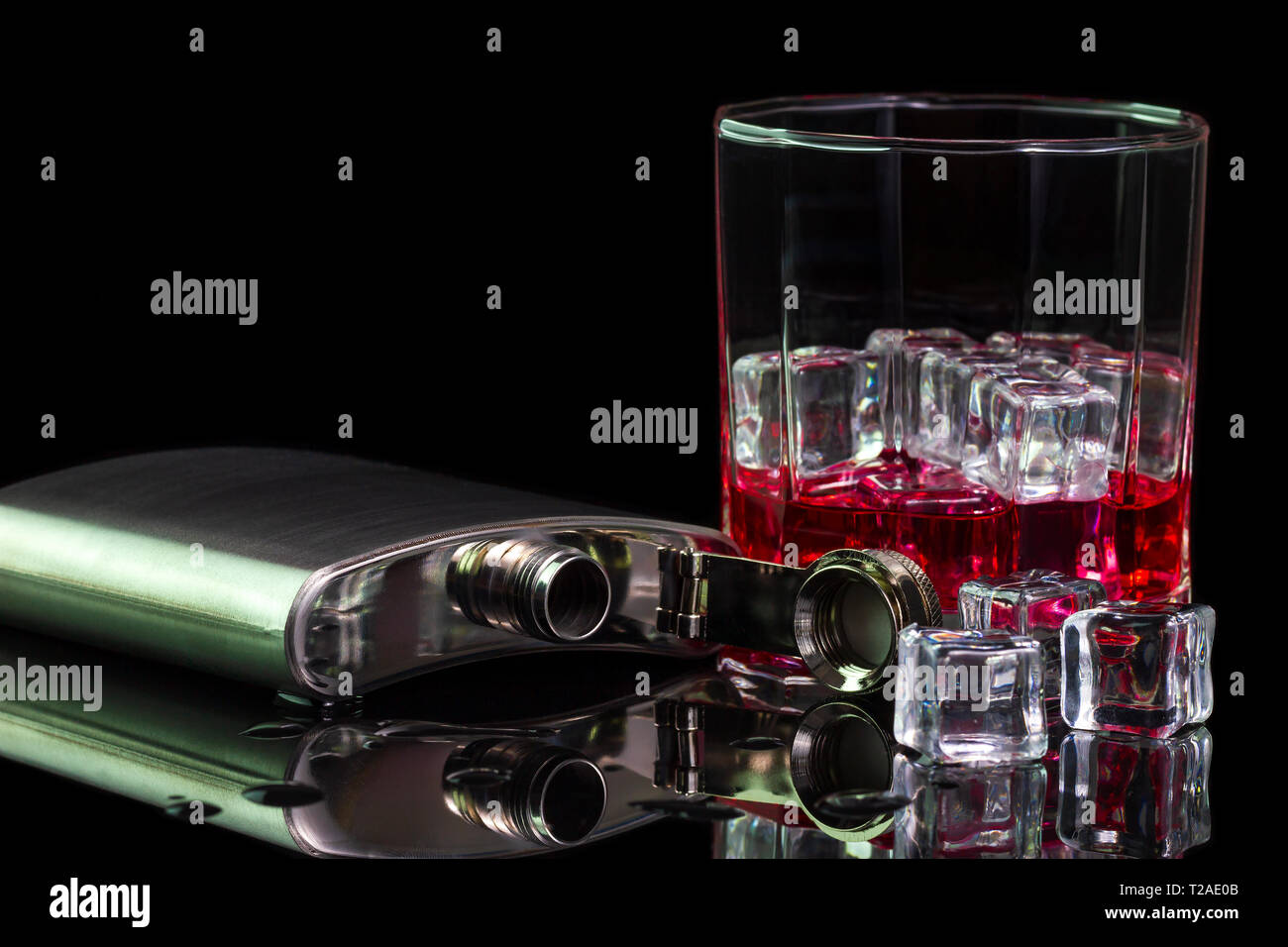 Stainless steel flask liquor alcohol and ice on table with red whiskey