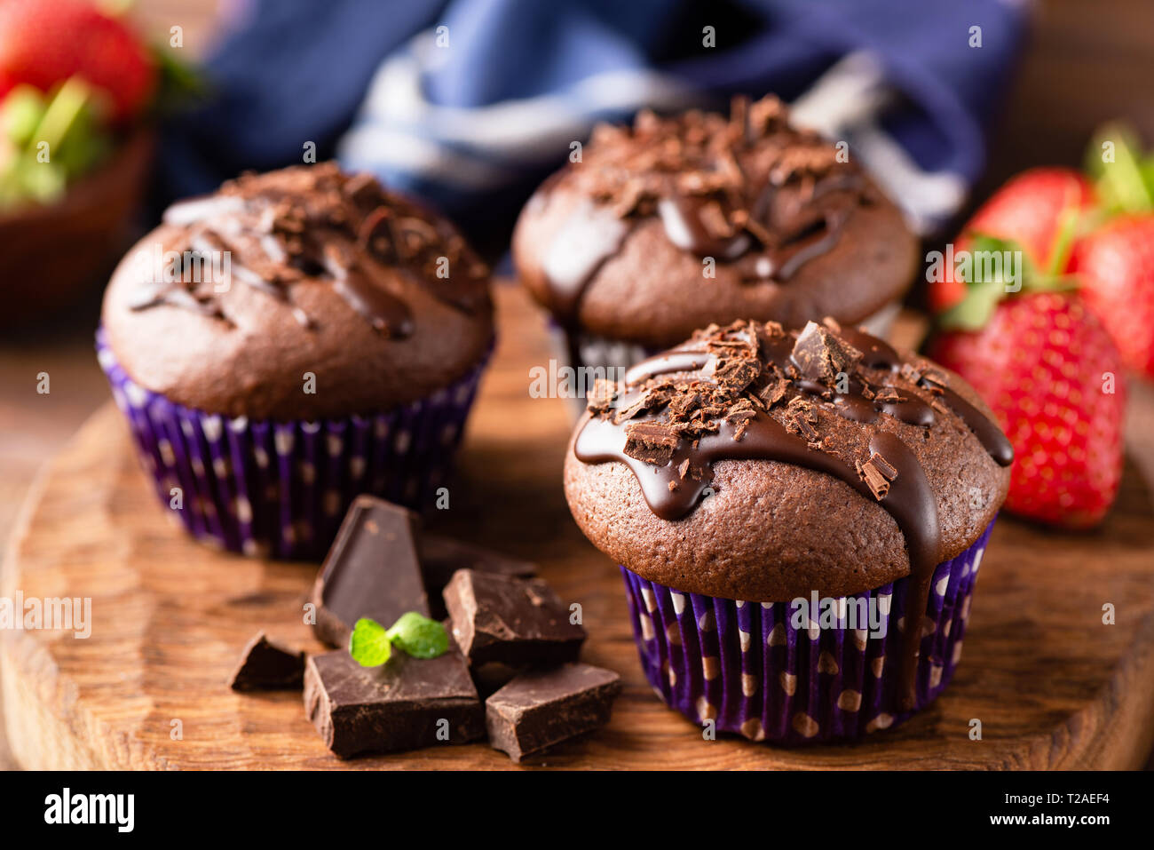 Tasty chocolate muffins glazed with chocolate ganache on a wooden serving board. Closeup view Stock Photo