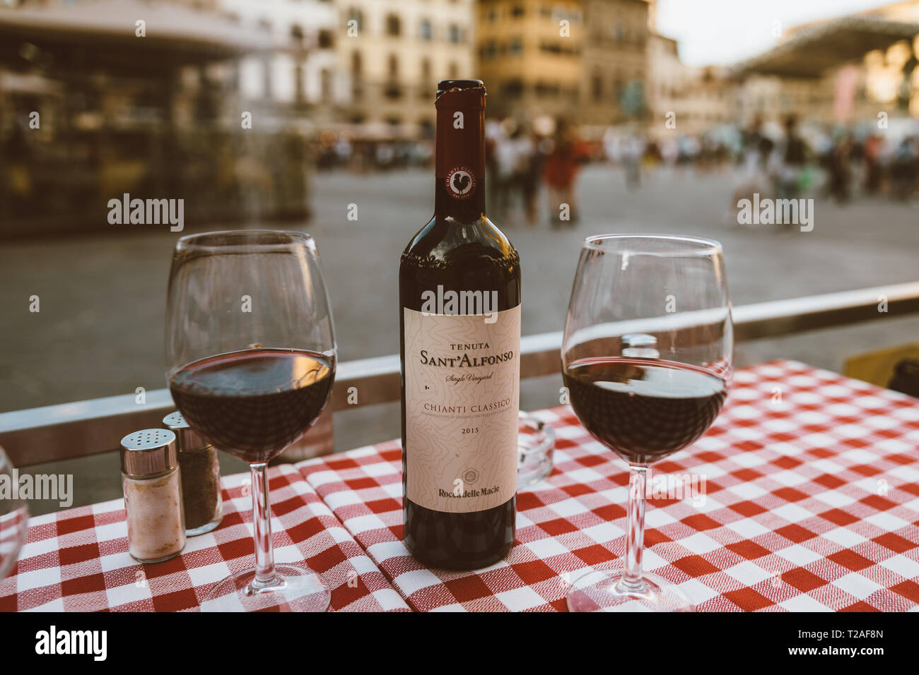 Florence, Italy - June 24, 2018: Closeup of bottle red wine Sant Alfonso Chianti Classico and glasses on table of restaurant on background of Piazza d Stock Photo
