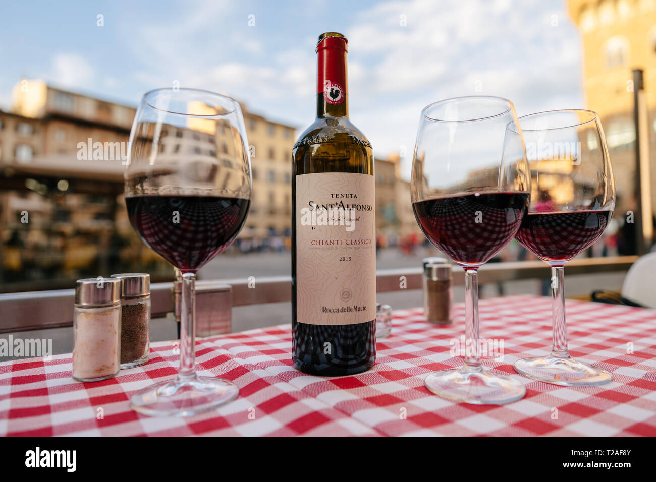 Florence, Italy - June 24, 2018: Closeup of bottle red wine Sant Alfonso Chianti Classico and glasses on table of restaurant on background of Piazza d Stock Photo