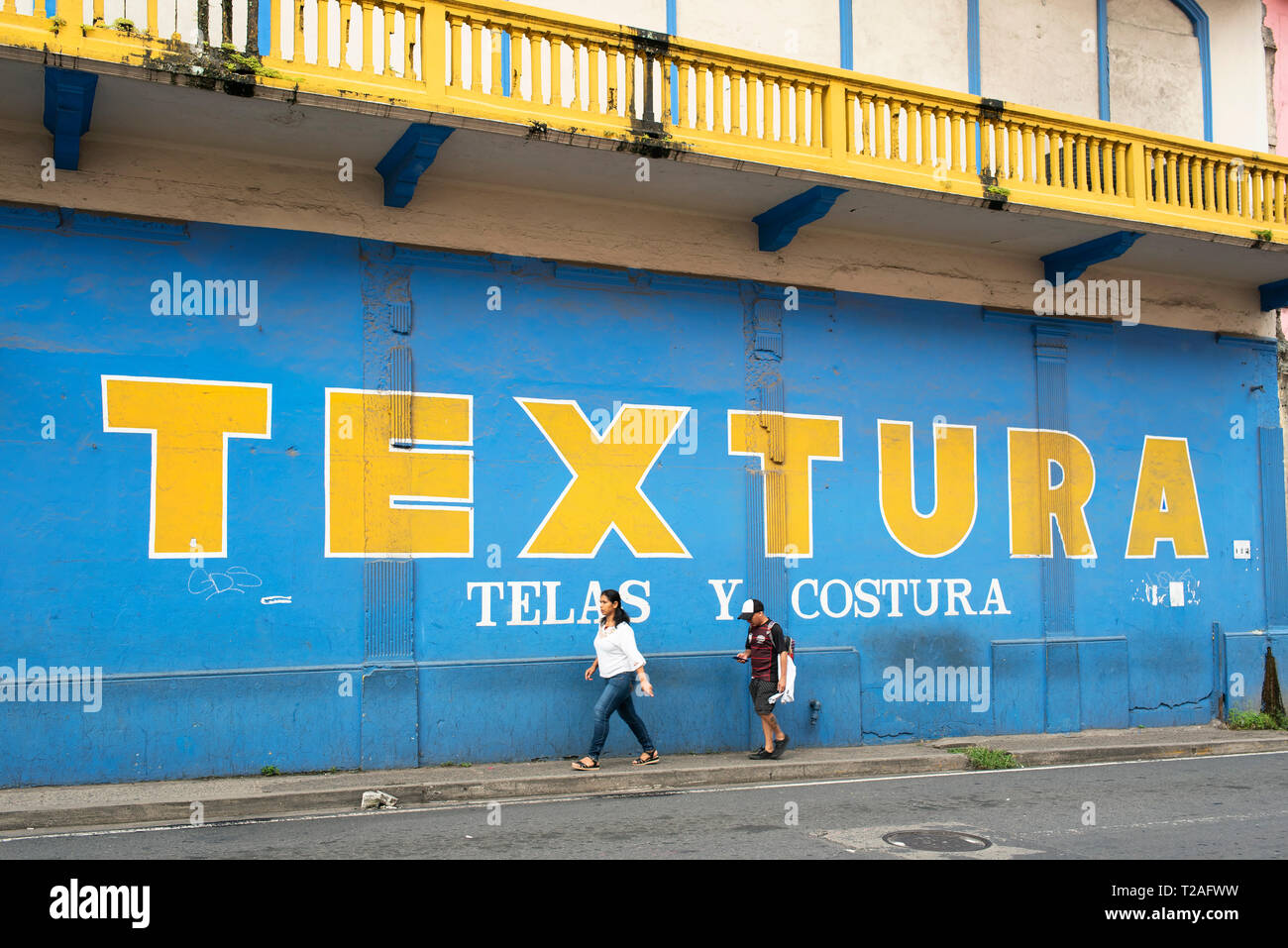 Street scene with people walking past a colourful wall of a fabric and sewing factory. Typography in Panama City, Panama, Central America. Oct 2018 Stock Photo