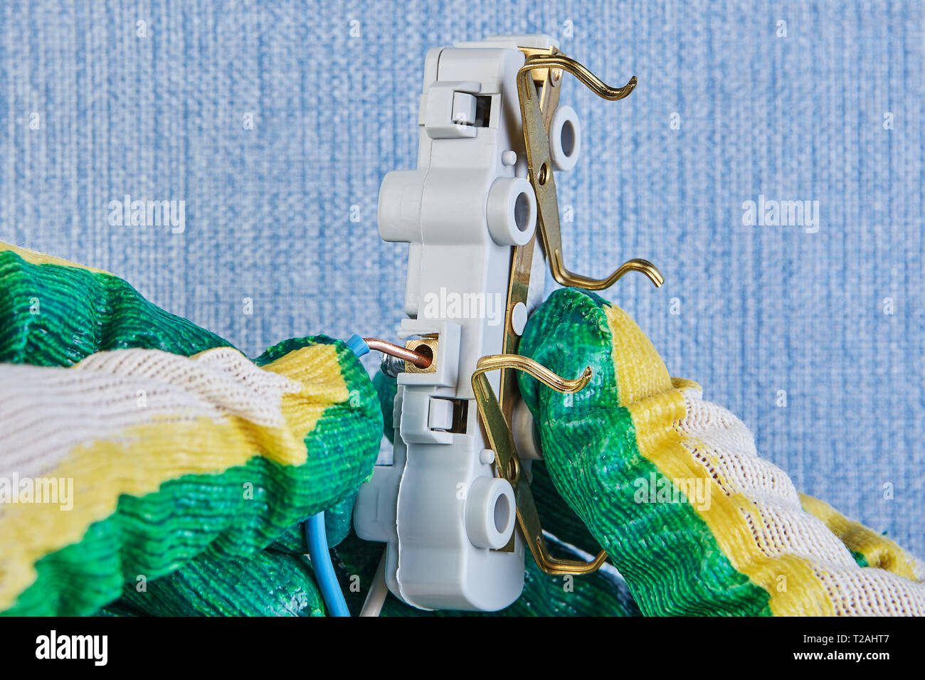 Electrician in protective gloves is inserting wires in electrical wall socket. Stock Photo