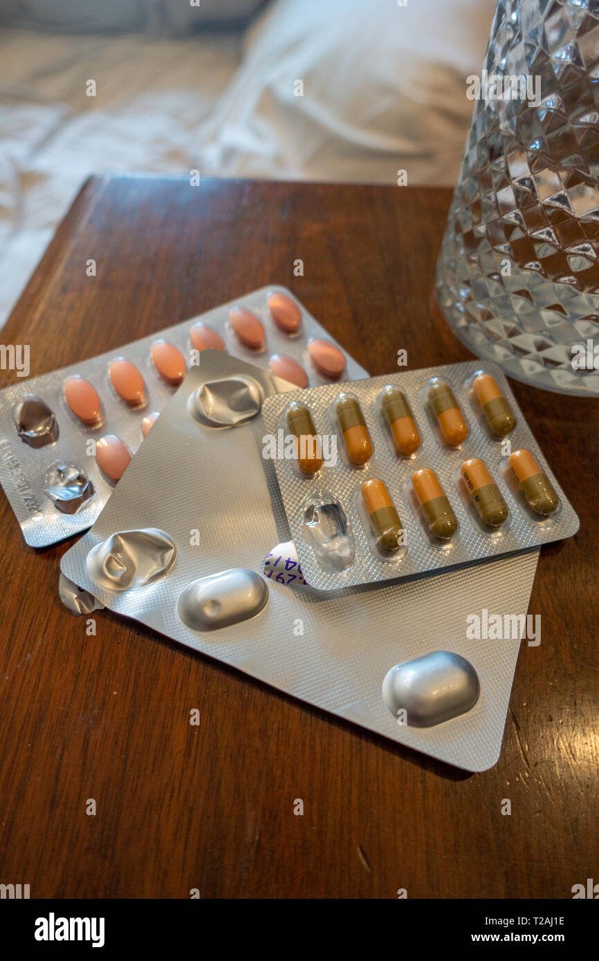 3 packets of Prescription drugs and a glass of water on a bedside table Stock Photo