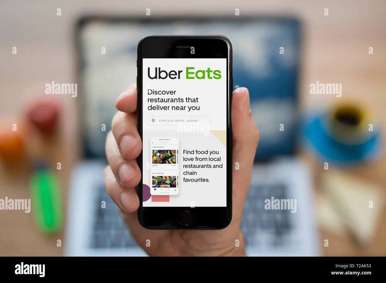 A man looks at his iPhone which displays the Uber Eats logo (Editorial use only). Stock Photo