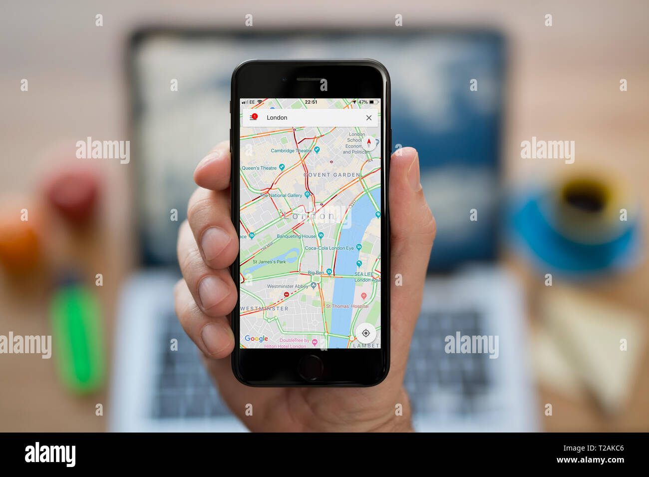 A man looks at his iPhone which displays the Google Maps logo (Editorial use only). Stock Photo