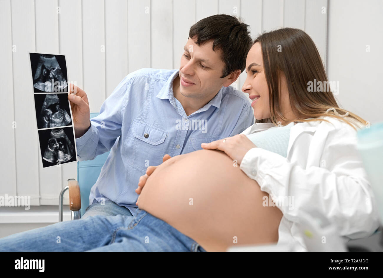 Side view of happy future mother and father sitting in clinic and looking at ultrasound image of baby photo