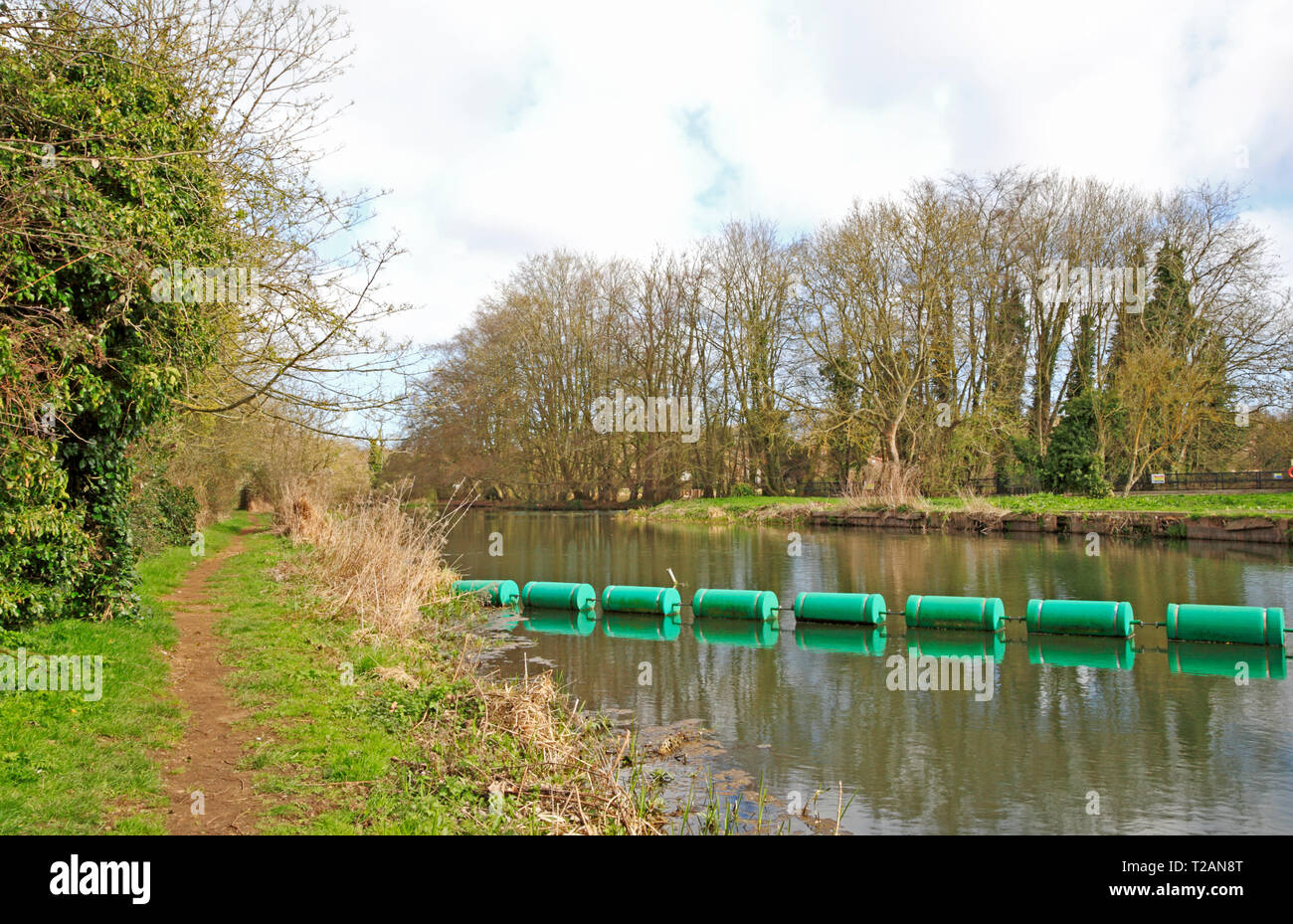 A view of the River Bure with boom and riverside footpath upstream of the old mill at Horstead, Norfolk, England, United Kingdom, Europe. Stock Photo