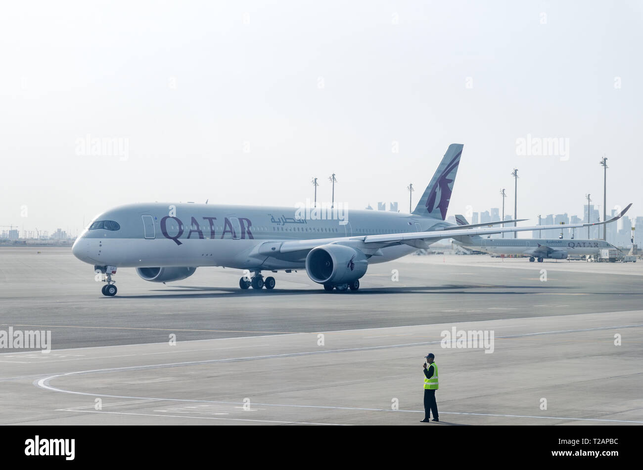 Doha, Qatar, 2018-05-01: Plane by Qatar Airlines leaves the parking lot. Marshaller controls the movement of the aircraft. Airport ground crew. Stock Photo