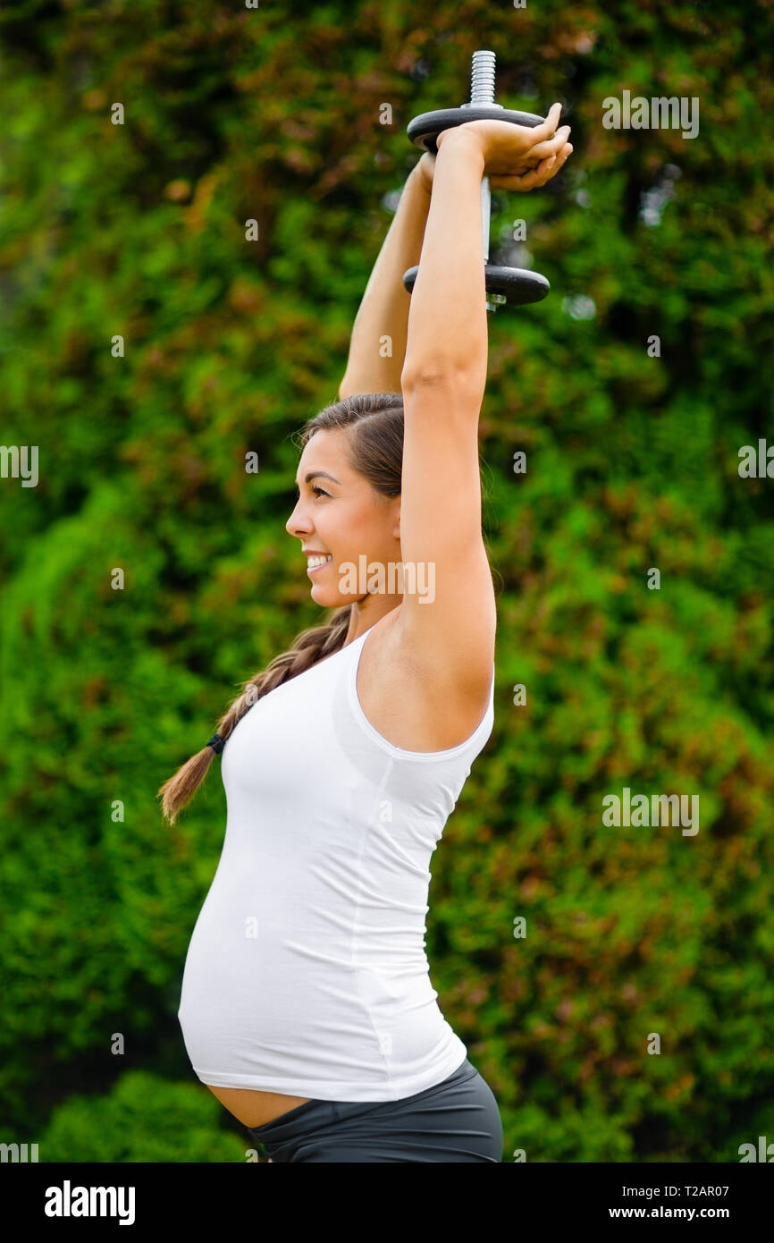 Smiling Pregnant Woman Doing Triceps Workout With Dumbbell In Park Stock Photo
