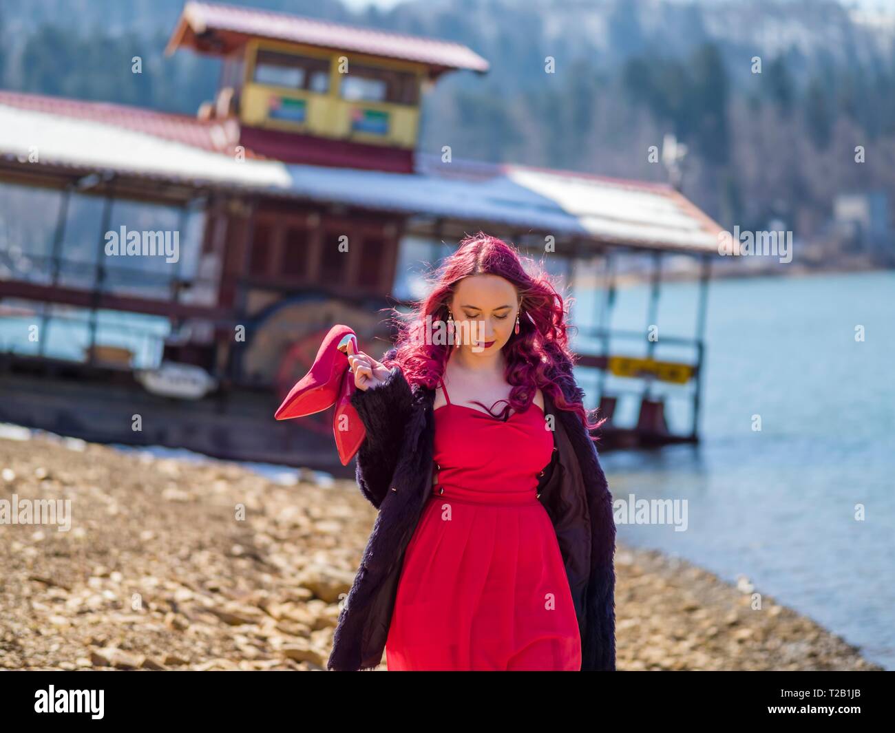 Young woman in 20s twenties outdoors in nature waking towards camera hand holding Red high-heeled heels stiletto shoes serious looking down MR Stock Photo