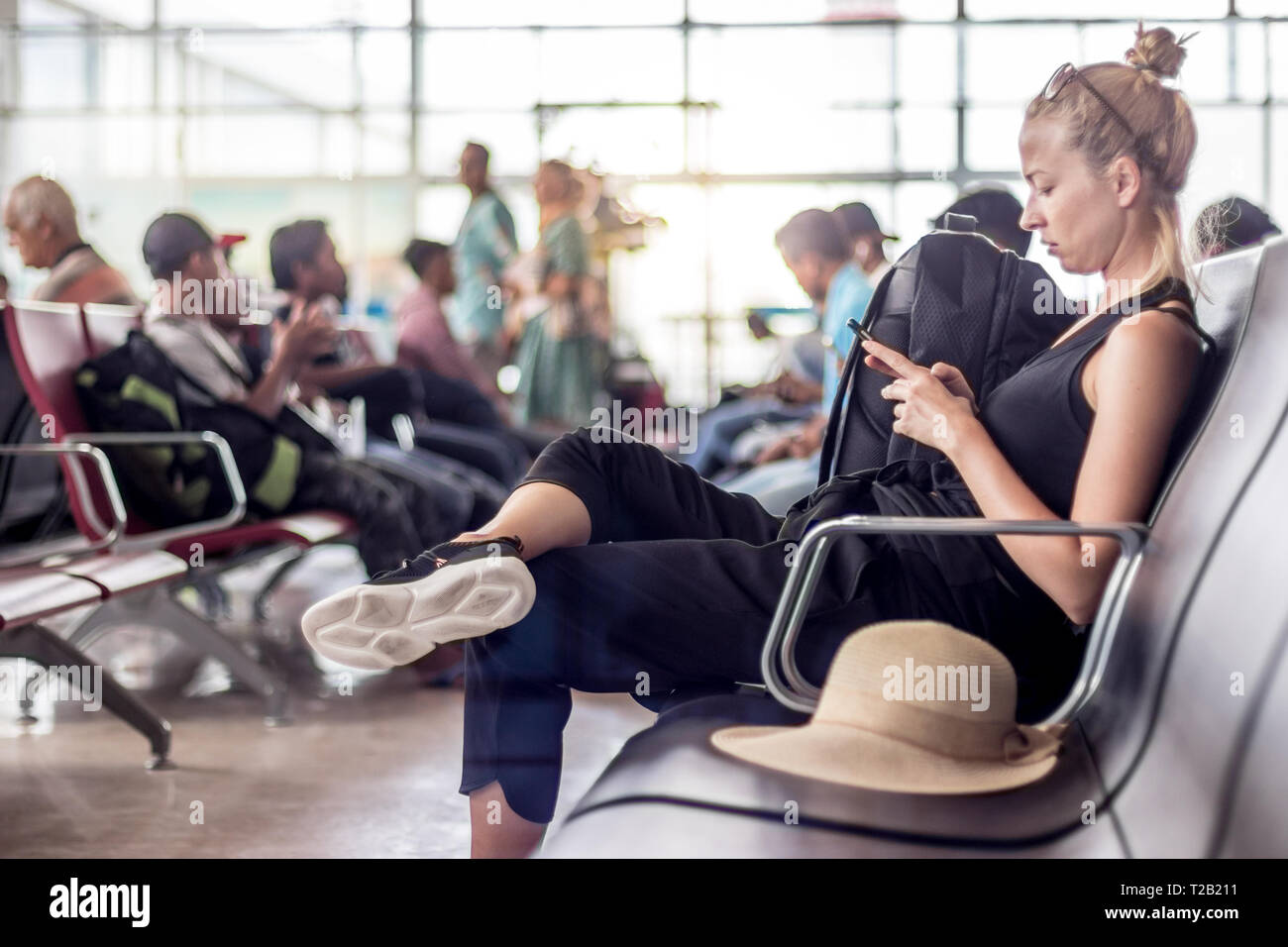 Female traveler using her cell phone while waiting to board a plane at departure gates at asian airport terminal. Stock Photo