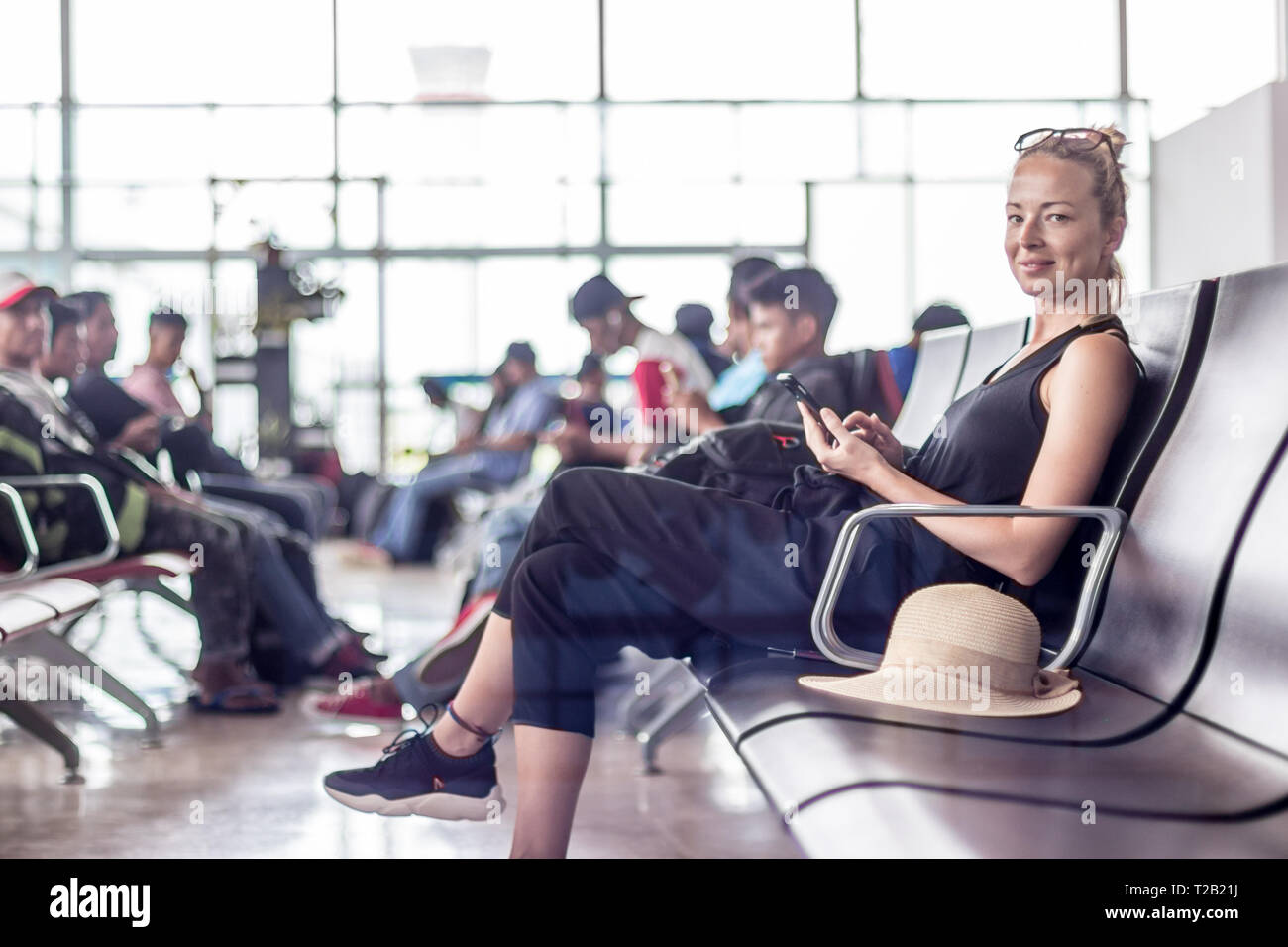 Female traveler using her cell phone while waiting to board a plane at departure gates at asian airport terminal. Stock Photo