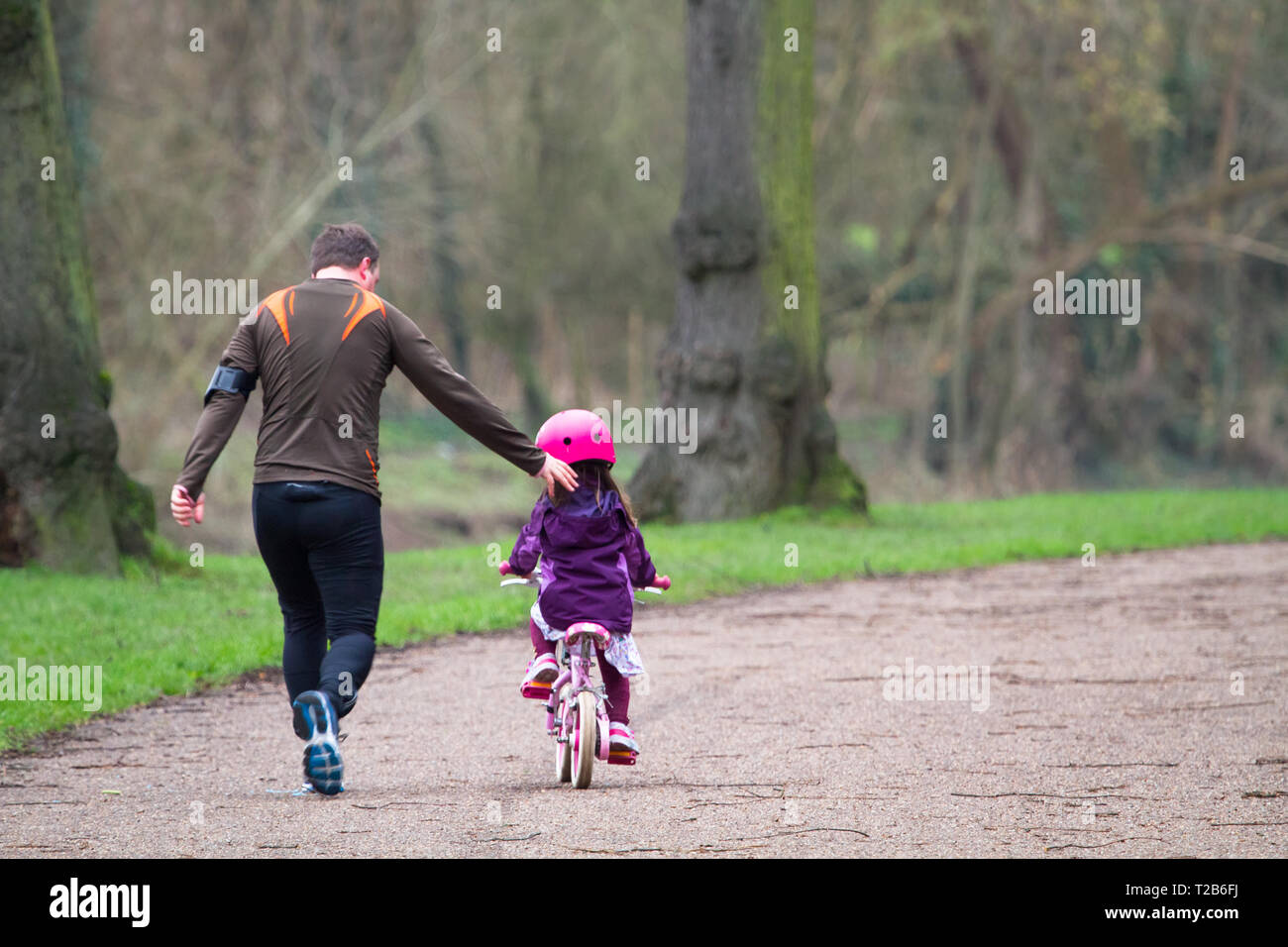 A father runs alongside his daughter who is learning to ride a bike in Shrewsbury, Shropshire, England. Stock Photo