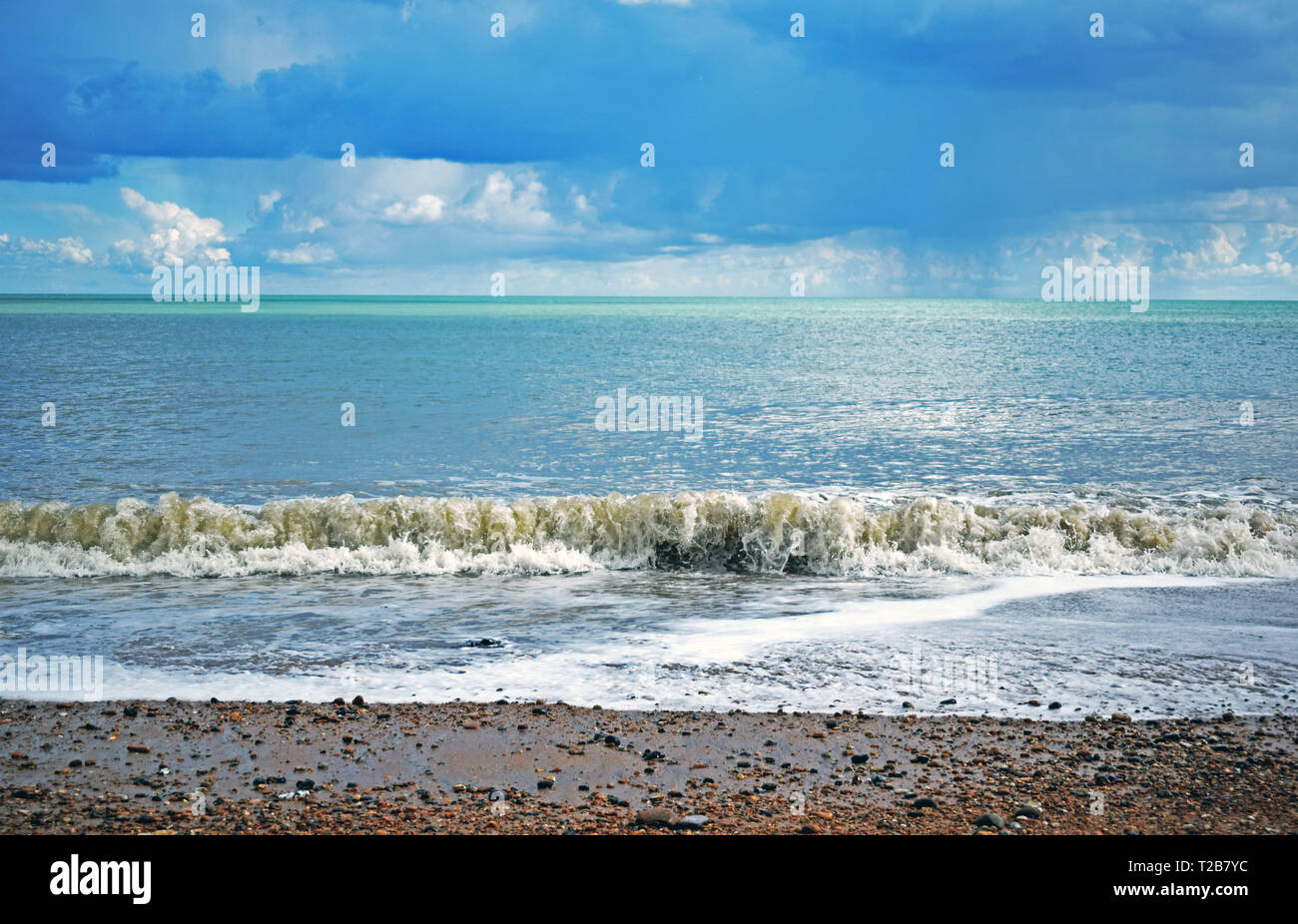 Sea scene with the waves coming up onto the pebble beach with a dramatic cloudy sky background Stock Photo
