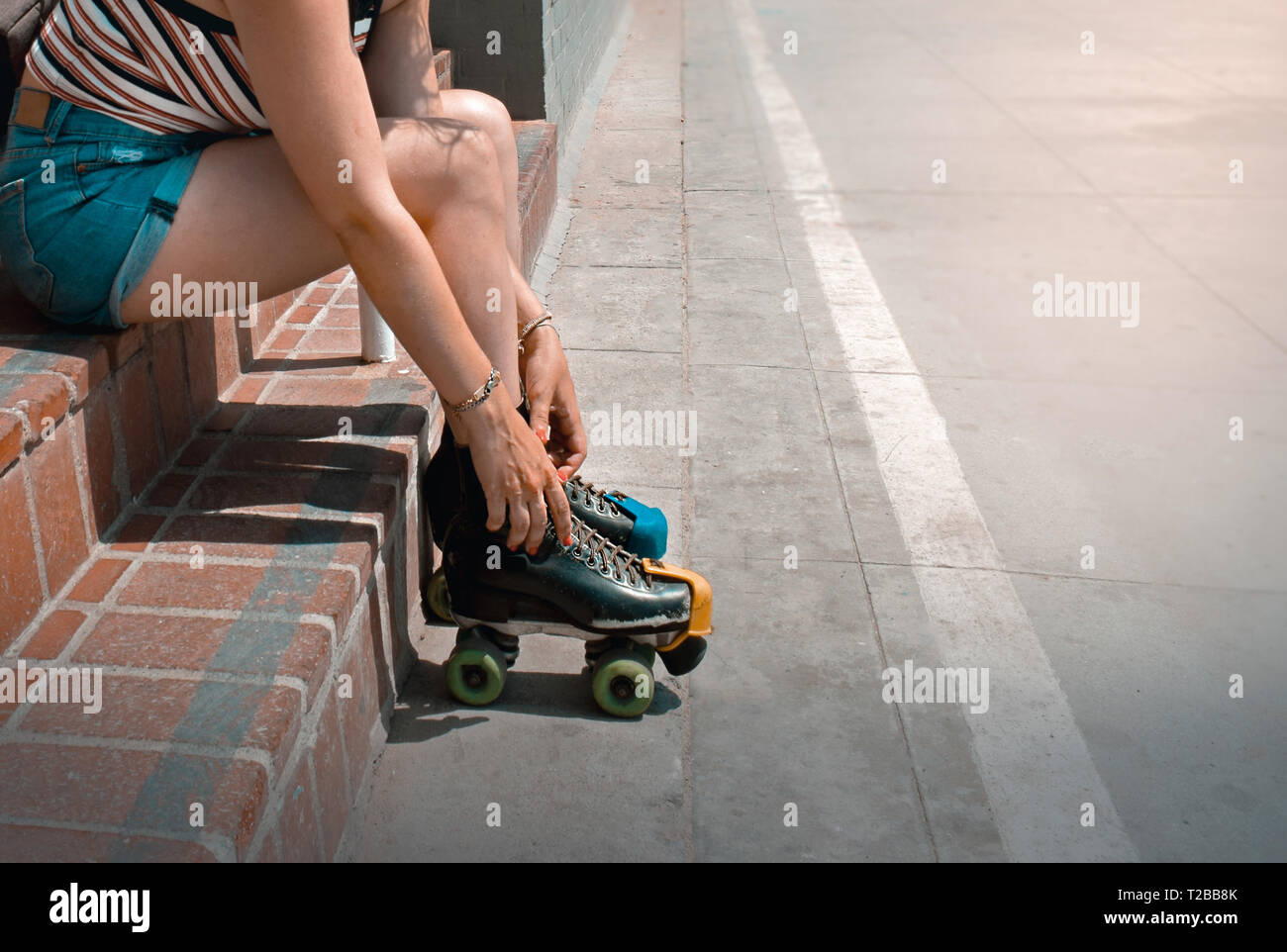 Girl seated at stairs tying roller skates at Venice Beach, Los Angeles, California, USA. Summer trendy lifestyle. Roller skate rent. Stock Photo