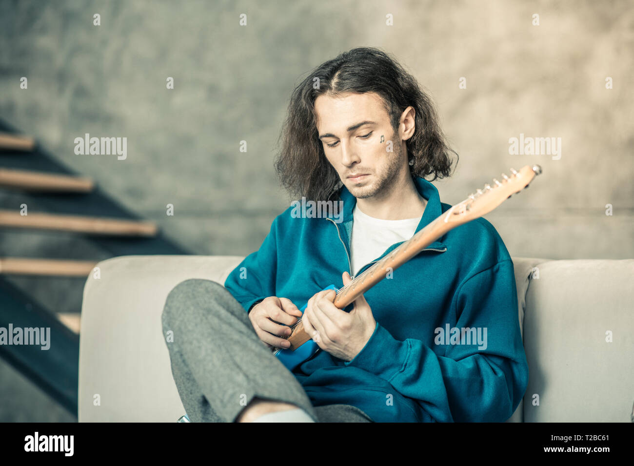 Curious young man with tattoo in his cheek setting up musical instrument Stock Photo