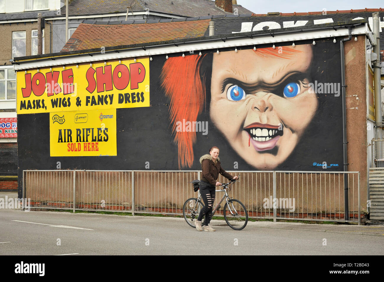 Women pushing bike past poster with image of evil clown advertising joke shop Stock Photo