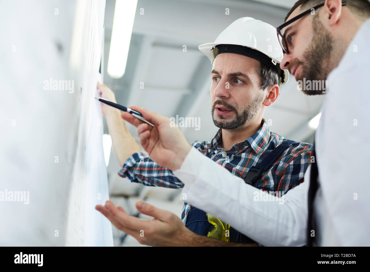 Low angle portrait of two factory workers discussing  plans standing in workshop, copy space Stock Photo