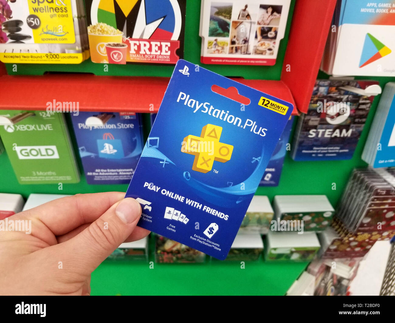 PLATTSBURGH, USA - JANUARY 21, 2019 : Play Station Plus 12 month membership gift card in a hand over a shelves with different giftcards in a Walmart s Stock Photo