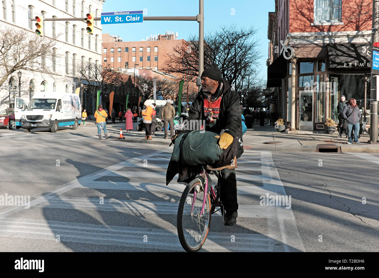 Black man on bicycle with belongings crosses at a crosswalk in the trendy Warehouse District neighborhood in downtown Cleveland, Ohio, USA. Stock Photo