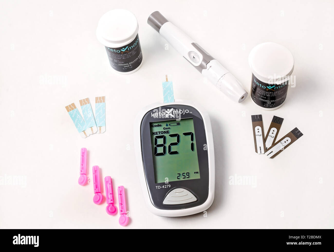 A Keto-Mojo ketone and blood glucose meter is pictured on white, along with ketone and glucose test strips, disposable needles, and lancet device. Stock Photo