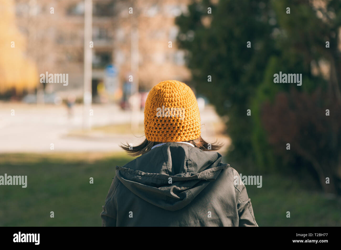 Rear view of casual female person walking on street in sunny spring morning Stock Photo