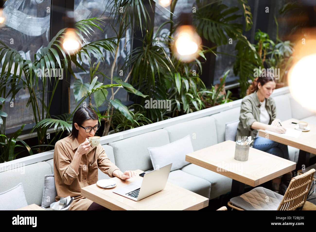 Lady drinking coffee while working in cafe Stock Photo