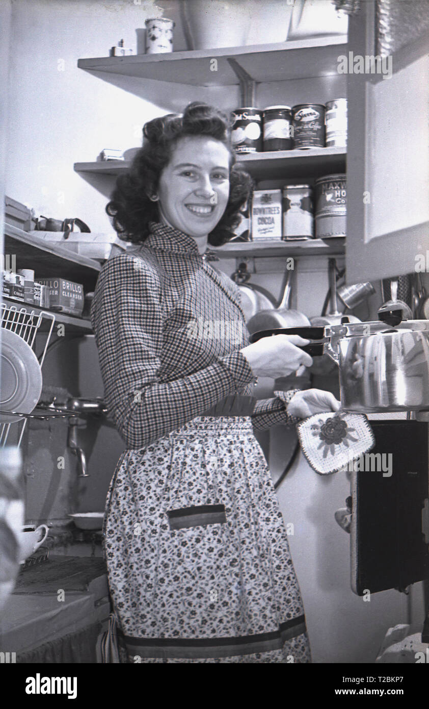 1940s, historical, happy lady in her apron, working in her tiny, compact kitchen or kitchenette. Stock Photo